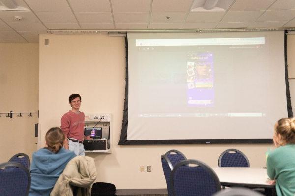 Caleb White stands to the left of a projection screen that shows a phone Spotify listing of Taylor Swift.