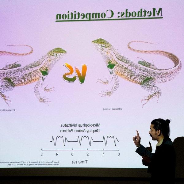 A person points at a screen showing images of two lizards with the word "vs" between them. At top are the words, "Methods: Competition."